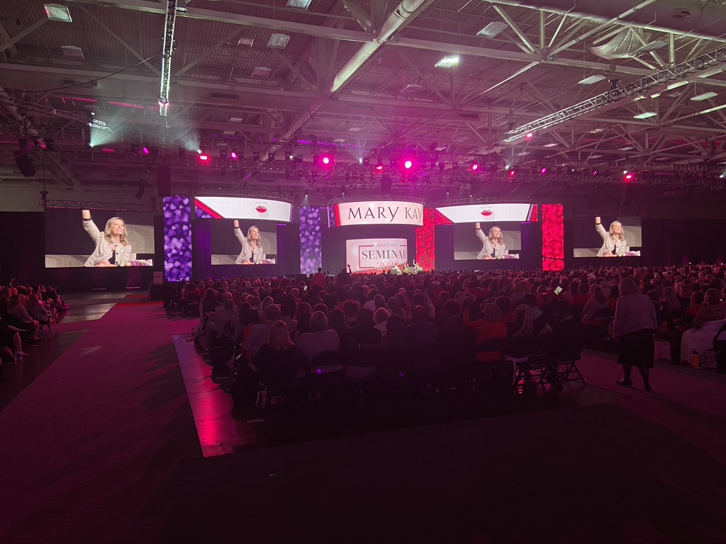 A light show over a stage and crowd at the Primerica International Convention with a large crowd and multiple screens reading “Primerica” and “Maximum Impact.”